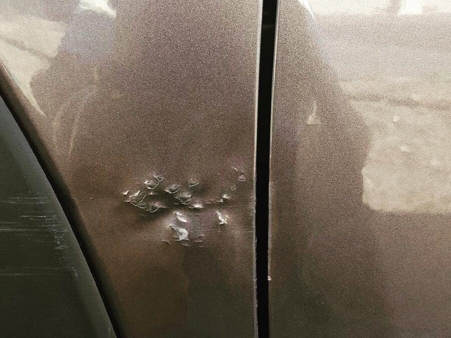 Car door with paint broken from underneath and flaking away after aggressive pushing with non-professional PDR tools