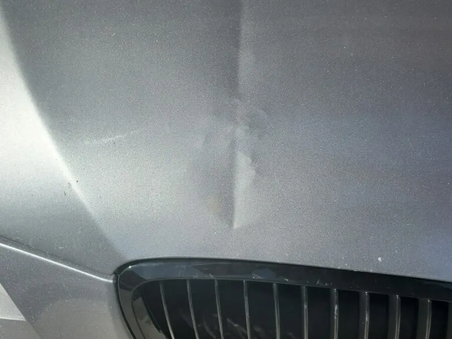 Clear coat cracked on a BMW hood after a dent was forced with the wrong tool