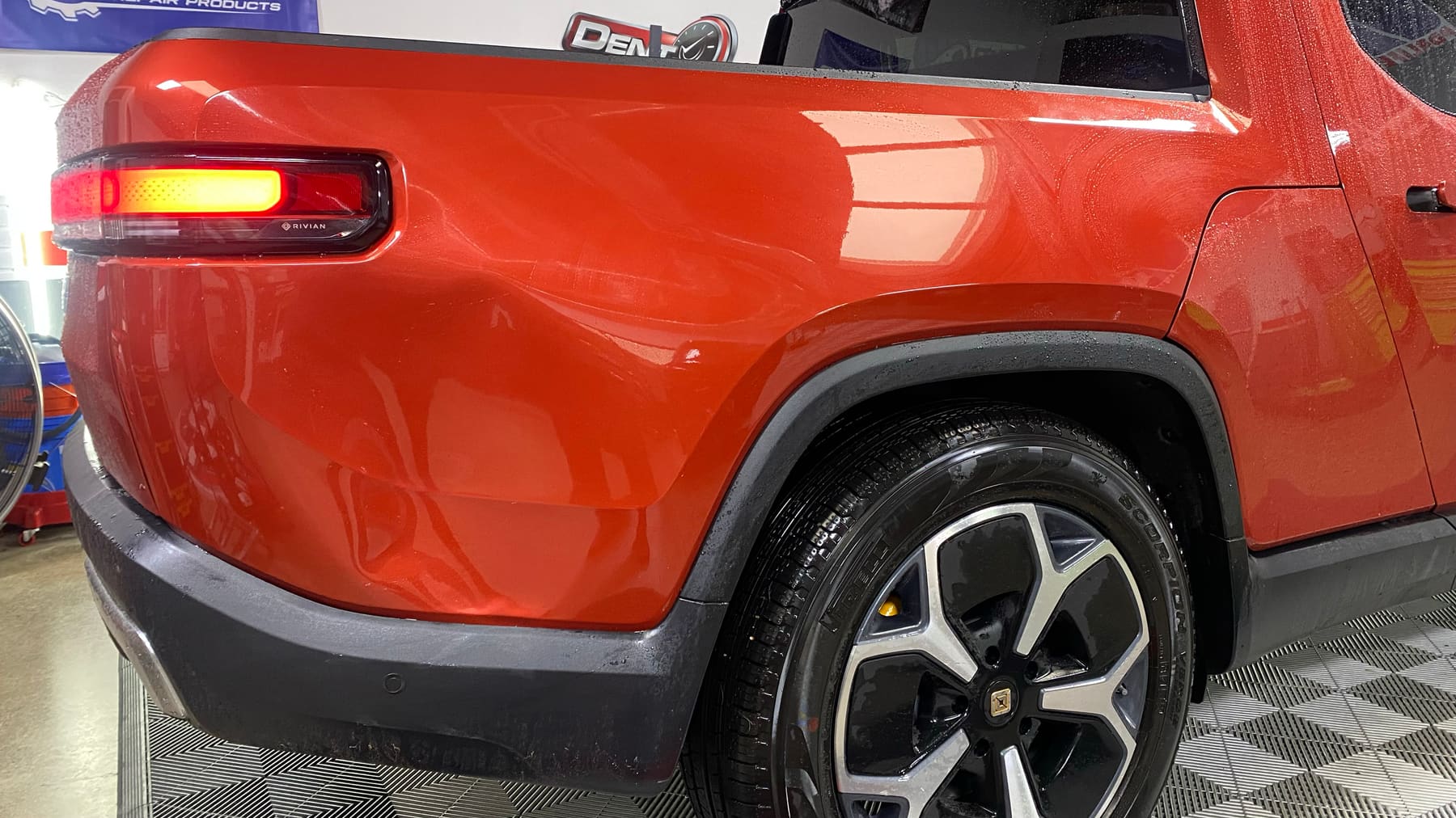 Deep smash across a red Rivian quarter panel before advanced large dent repair in San Diego