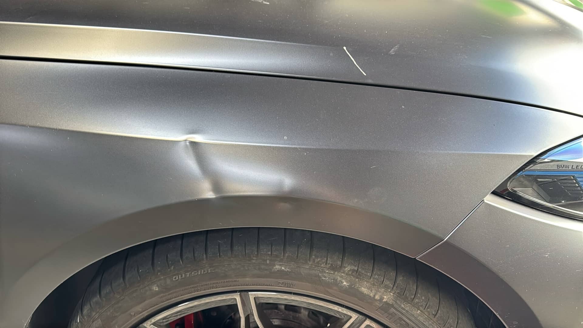 Matte BMW fender with a sharp crease dented into the body line before paintless dent repair