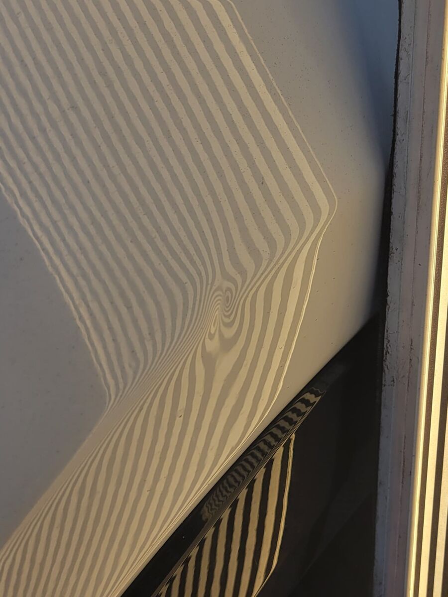 Reflection board lines collapsing into a tight whorl over a dent before paintless dent repair